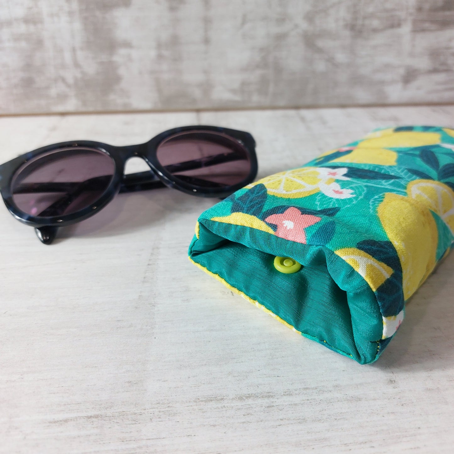 Close-up view of bold green and yellow Sicilian lemon print glasses case, pictured with sunglasses.