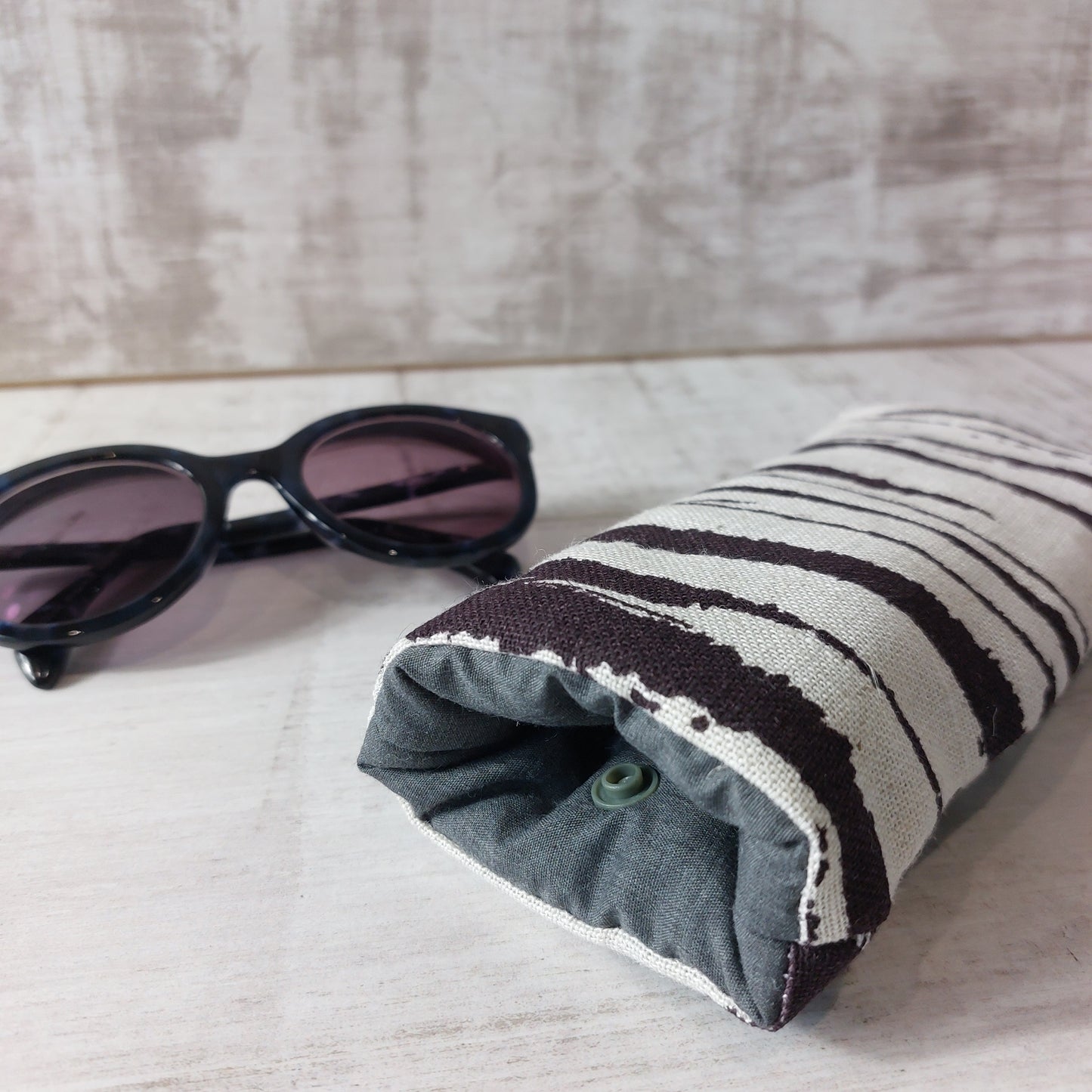 Closeup of chocolate brown and neutral linen sunglasses case showing snap fastening, with sunglasses.