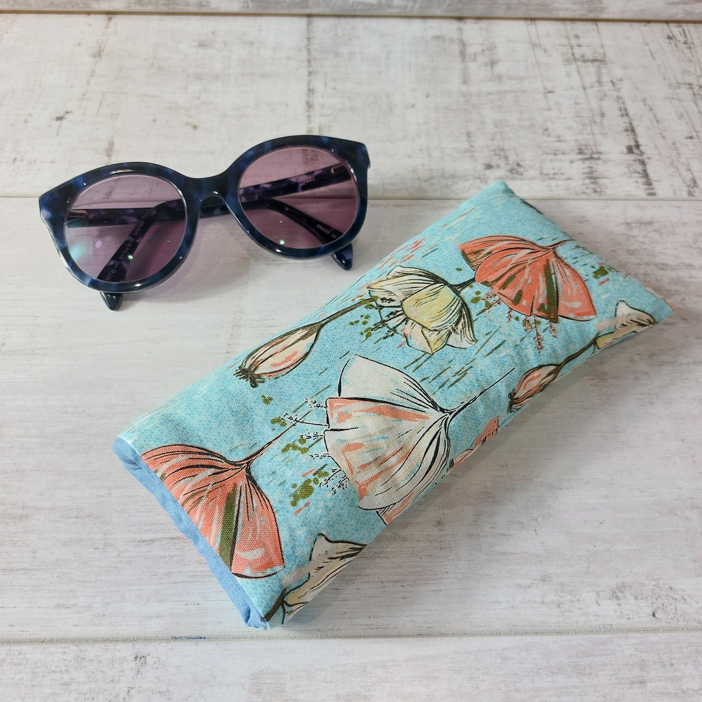 Blue stylised poppy print glasses case by Olganna, pictured with sunglasses.