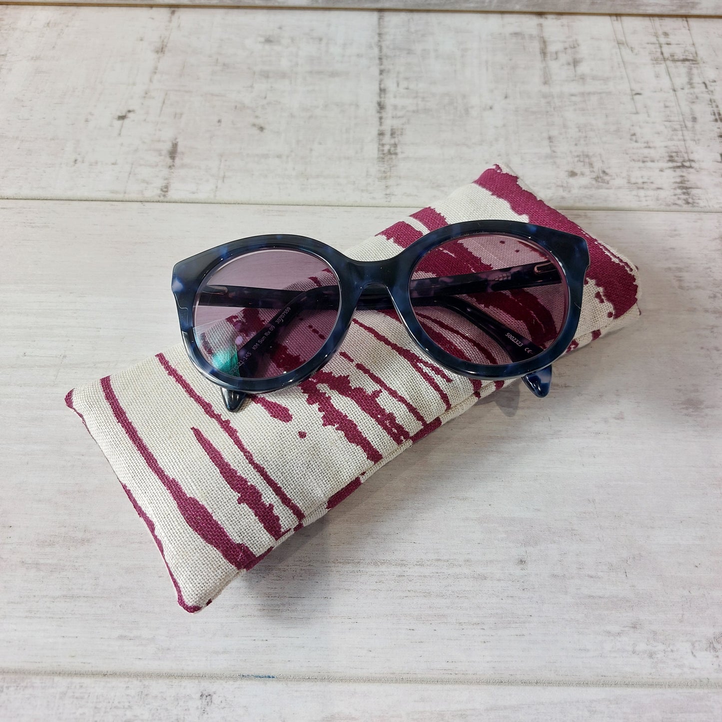 Wine and neutral linen sunglasses case with sunglasses resting on top.