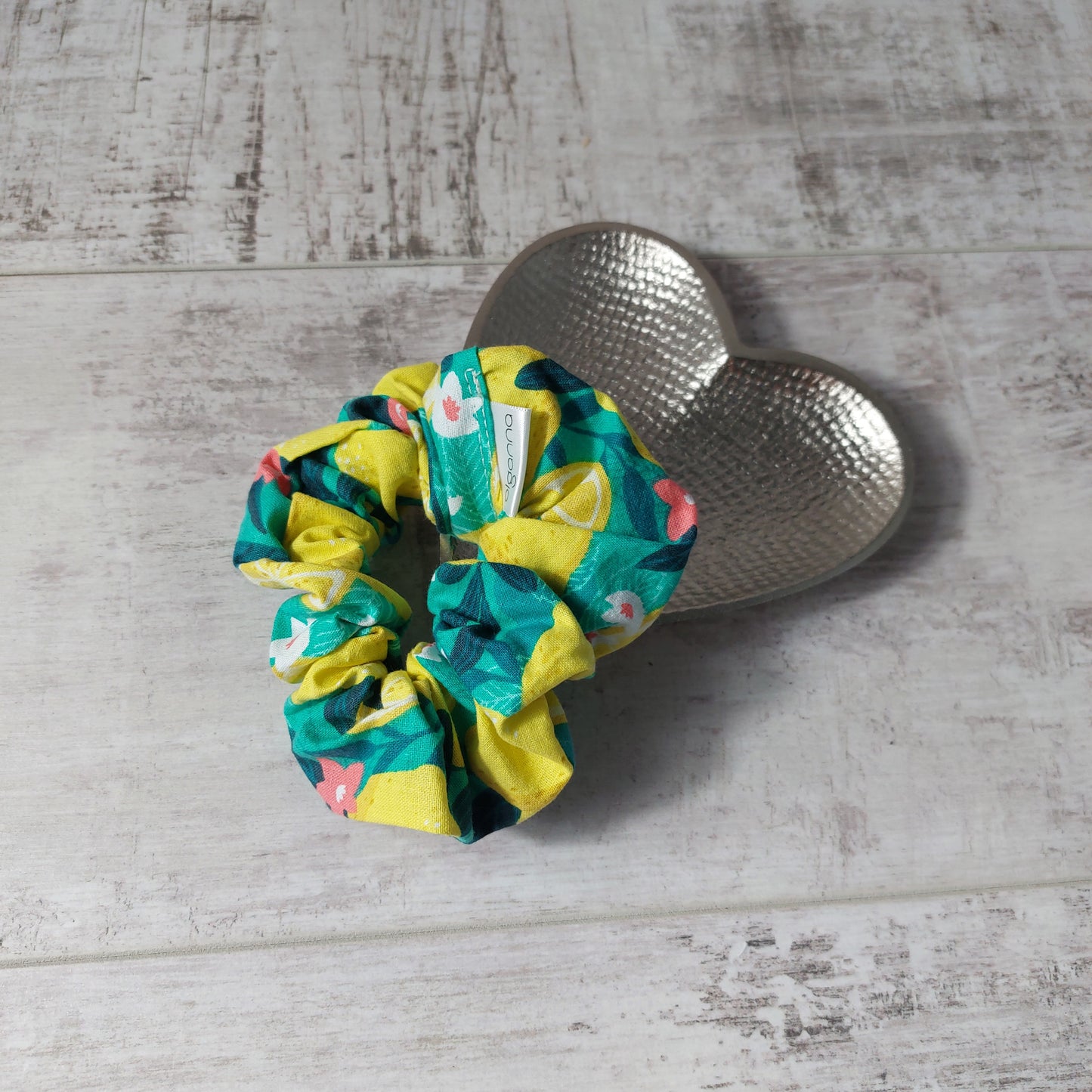 Bold green and yellow Sicilian lemon print hair scrunchie, pictured on a silver heart dish.