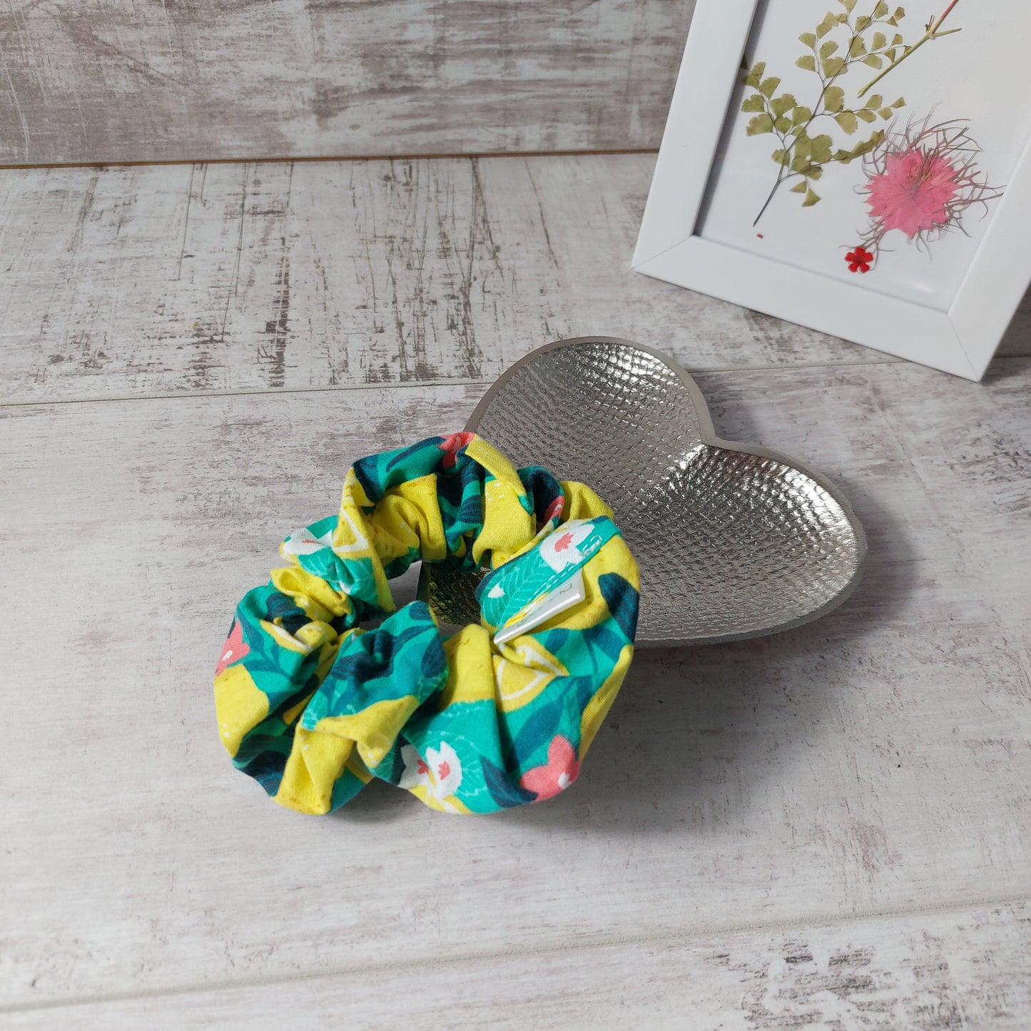 Bold green and yellow Sicilian lemon print hair scrunchie, pictured on a silver heart dish with a floral framed picture.