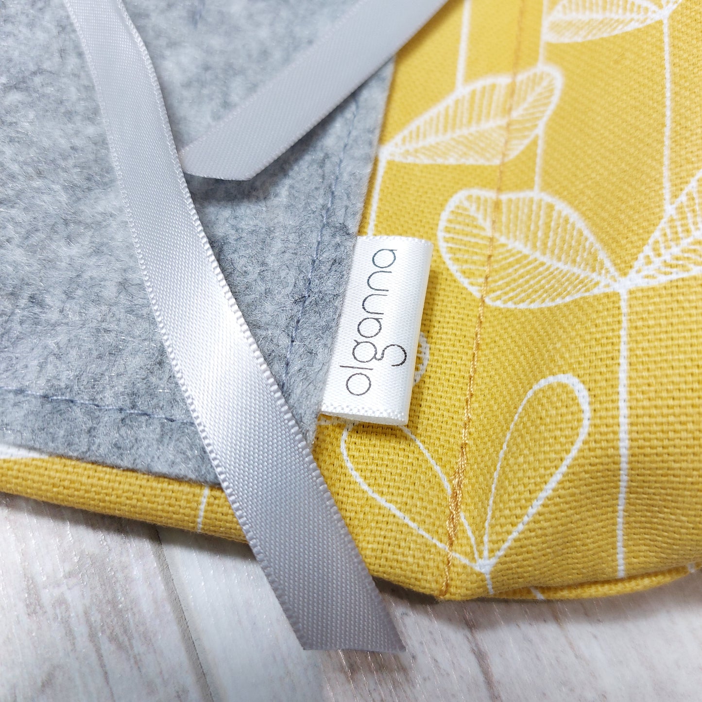 Closeup inner view of sunshine yellow makeup wrap with grey inner pocket, silver ribbon ties and 'olganna' label.