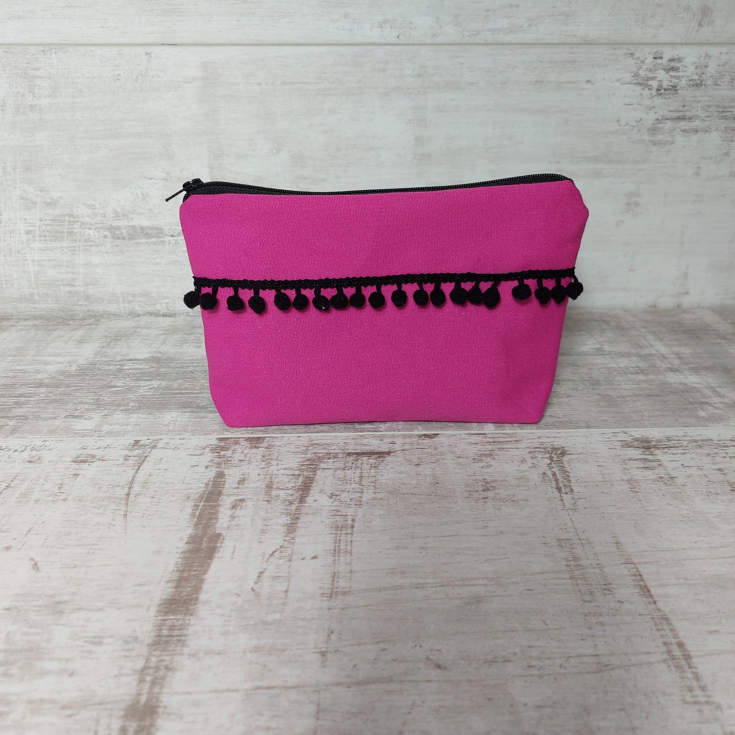 Hot pink canvas makeup bag, front view, with black pom poms.