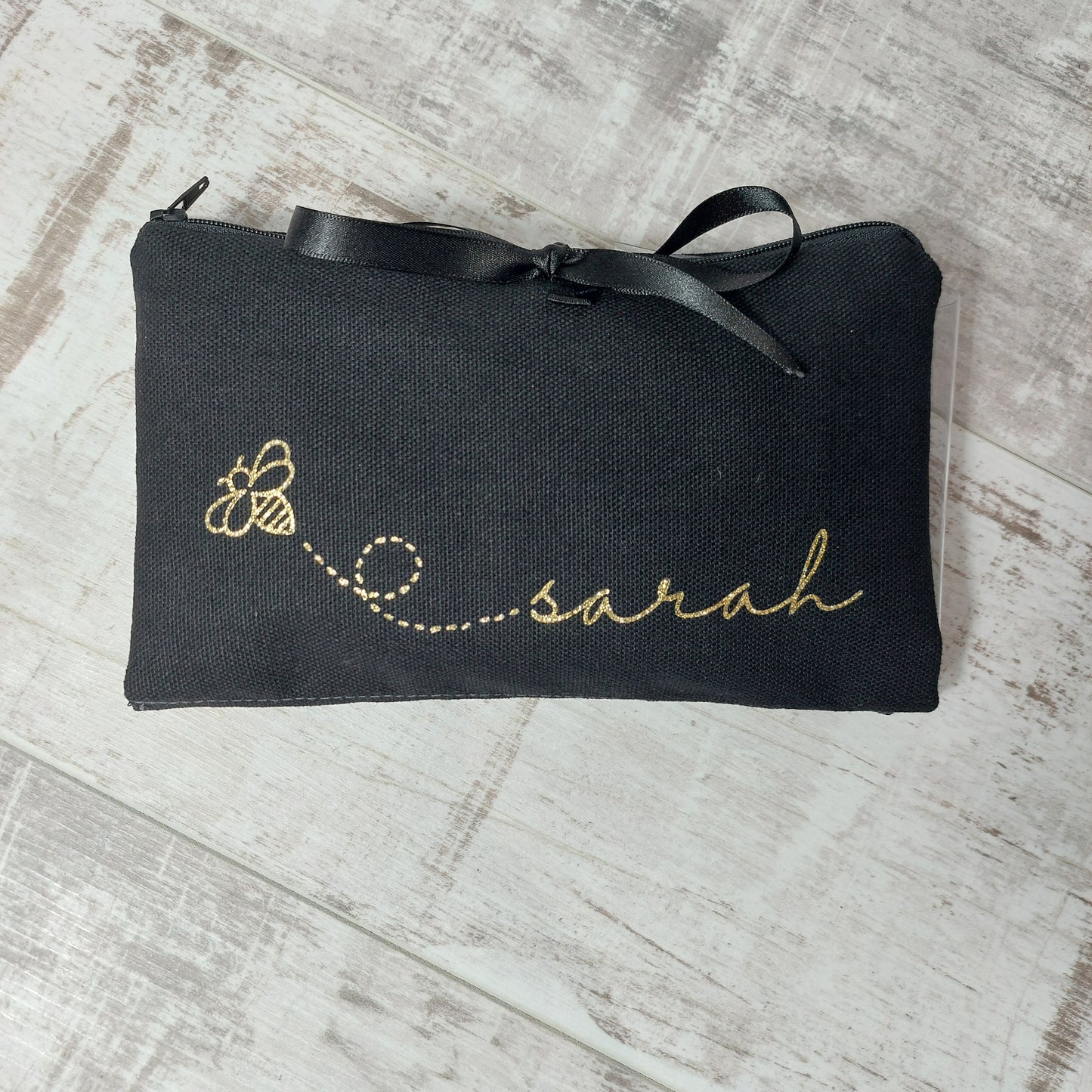 Black makeup wrap with gold glitter bee and personalised with the name 'Sarah' in gold, with black ribbon tie, by Olganna.