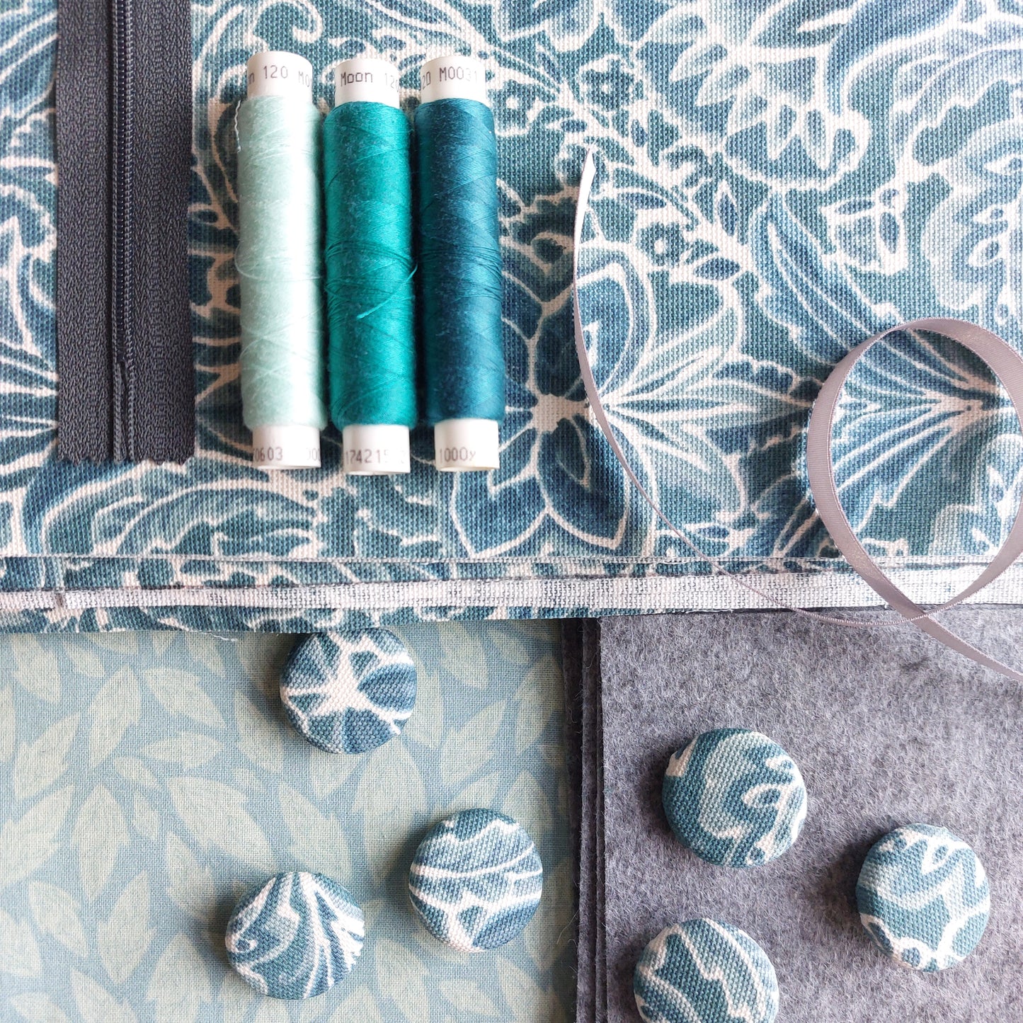 Teal print canvas fabric and buttons pictured with thread, zip and ribbon.