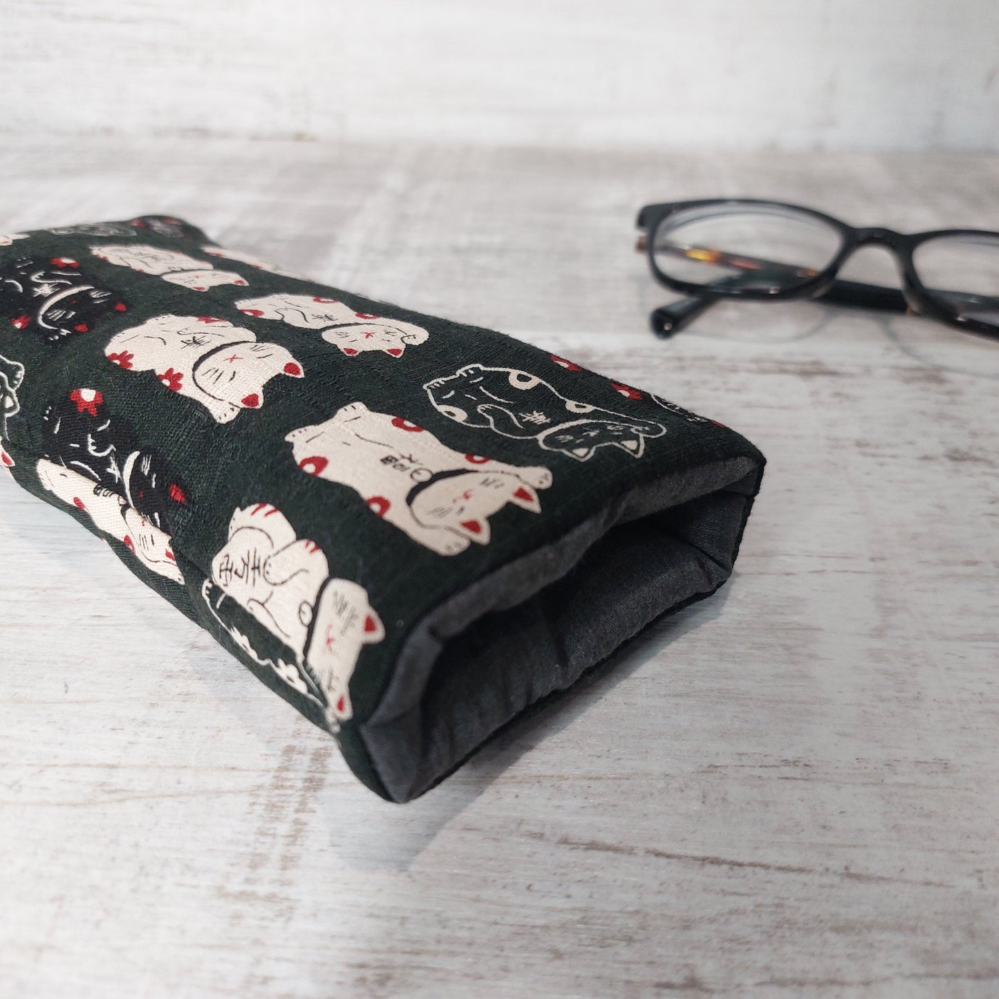 Close-up of black lucky cat glasses case showing padded black lining, pictured with glasses.