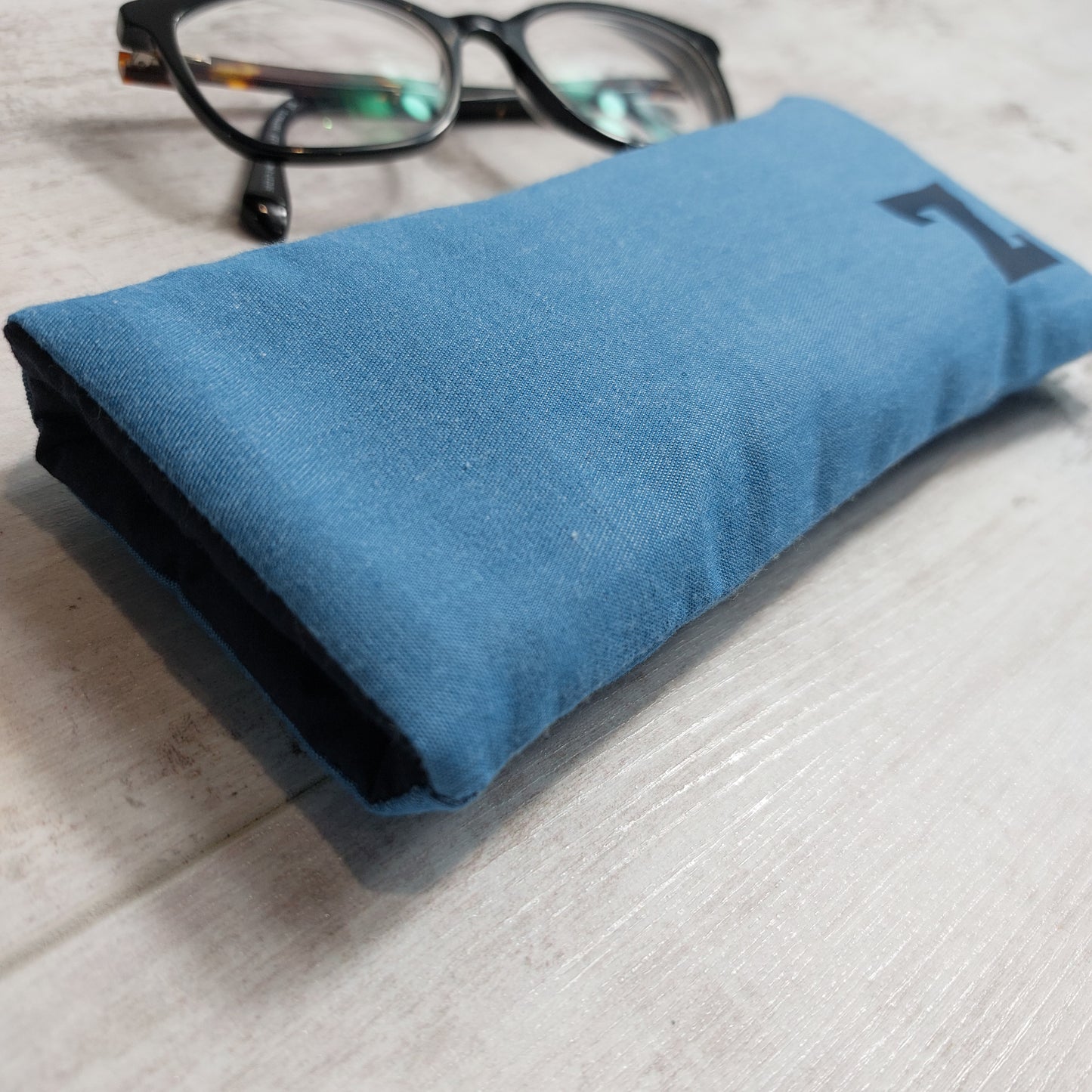 Side view of light blue fabric glasses case with 'Z' initial applied in contrast navy print, with glasses in the background.