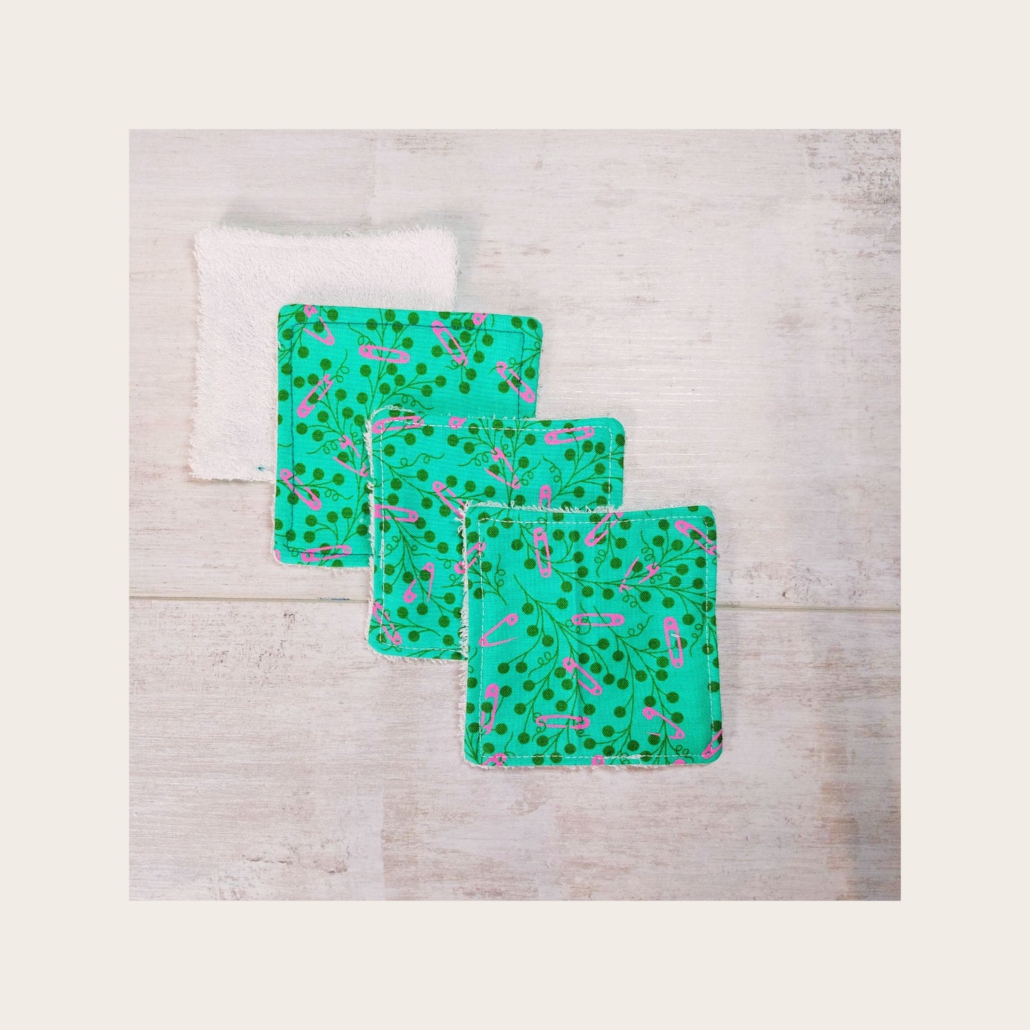 Four bamboo face wipes overlapping, in teal floral print with pink safety pin detail, by Olganna.