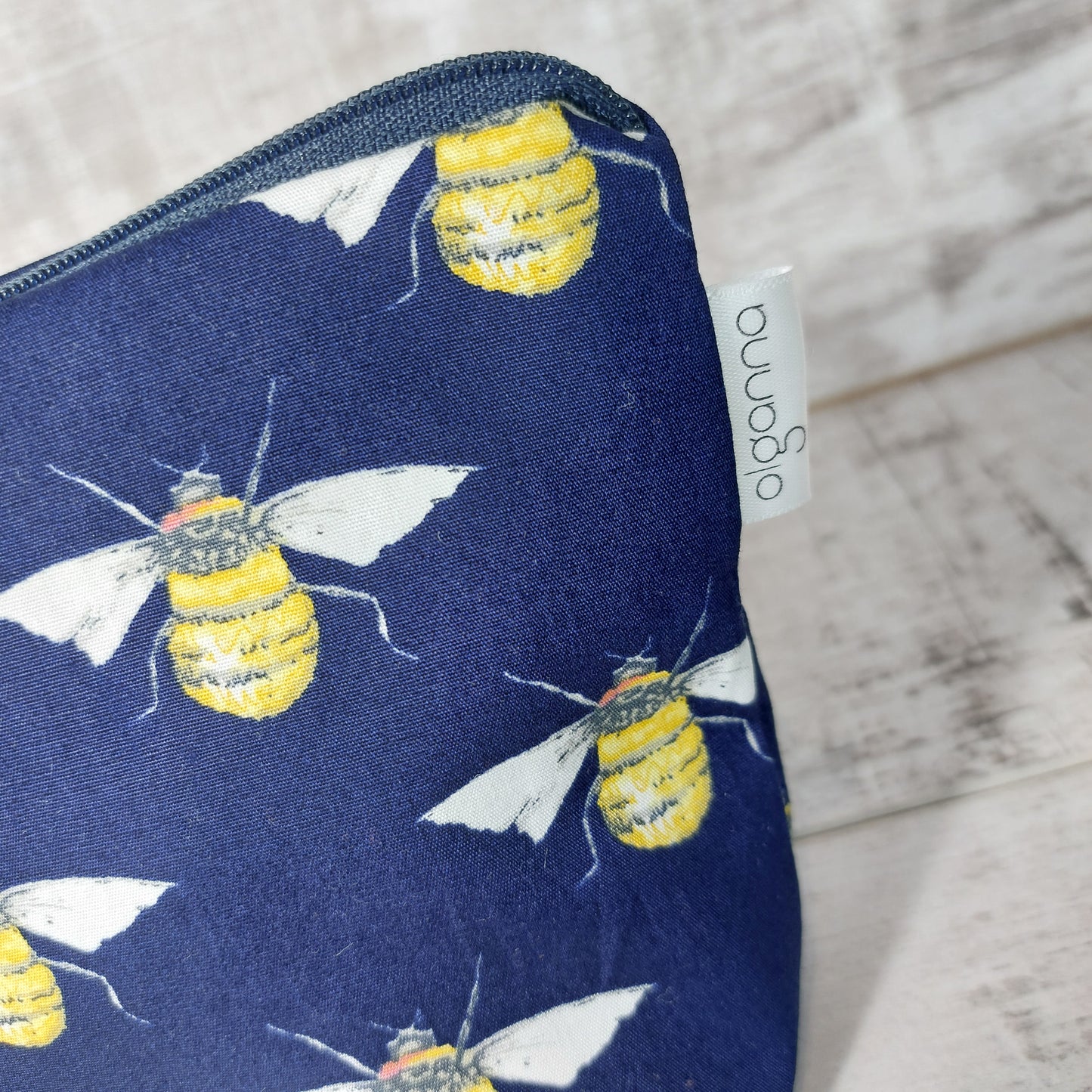 Close-up view of navy bee print makeup bag with side label saying 'olganna'.