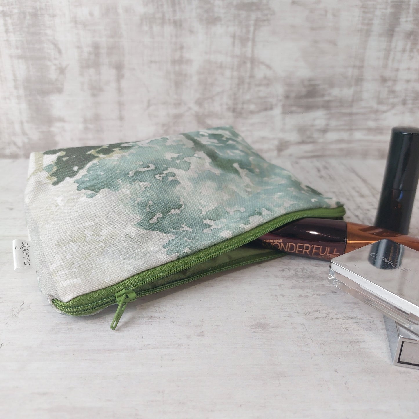 Make up bag in Forest Green Tree Print with green zip fastening, lying open next to beauty essentials.