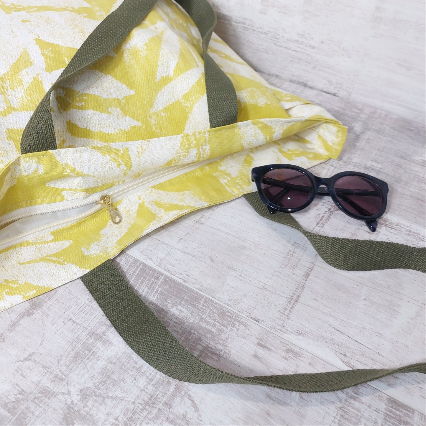 Bright citrus yellow leafy print beach bag, lying down, pictured with sunglasses.