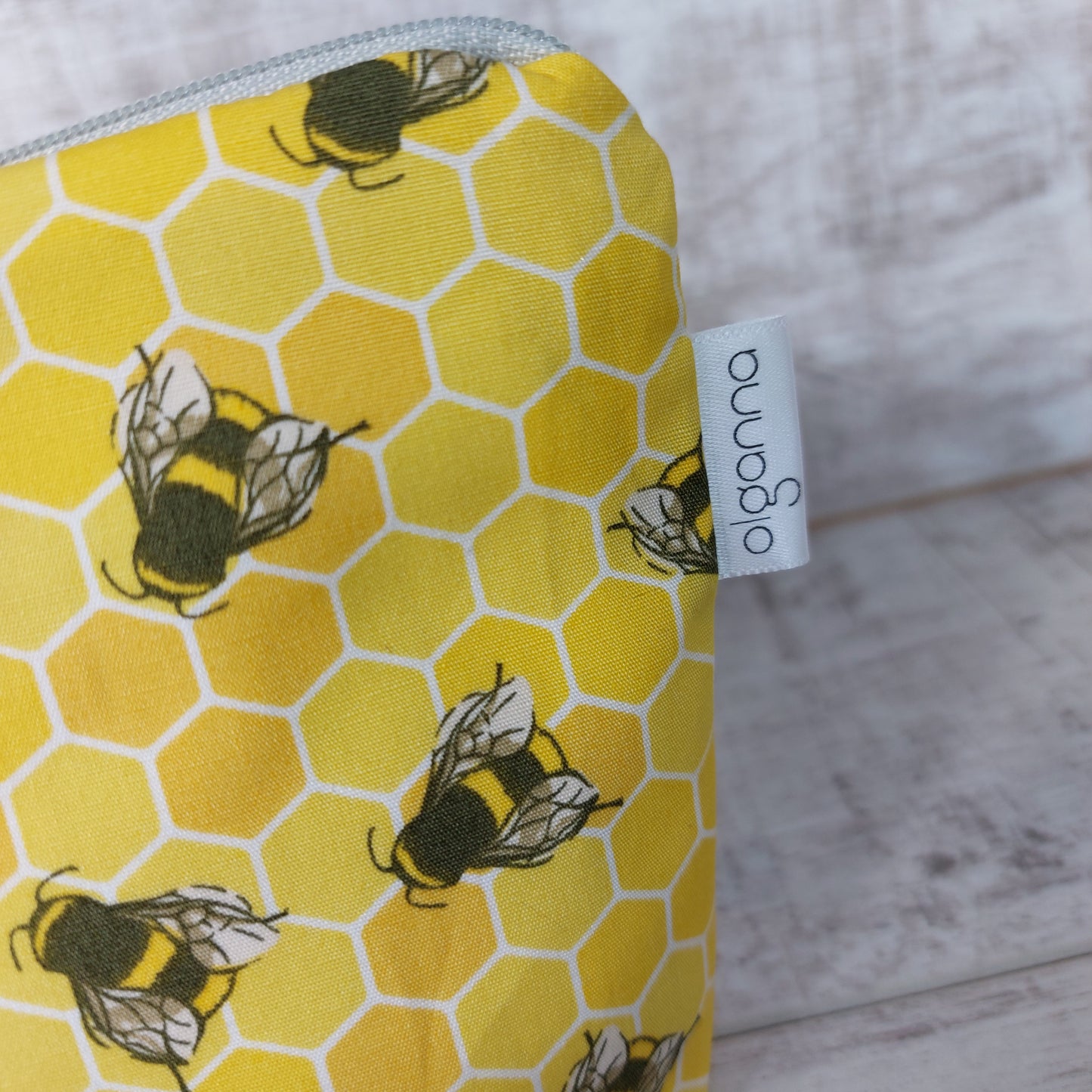 Close-up view of makeup bag in yellow honeycomb bee print with side label saying 'olganna'.