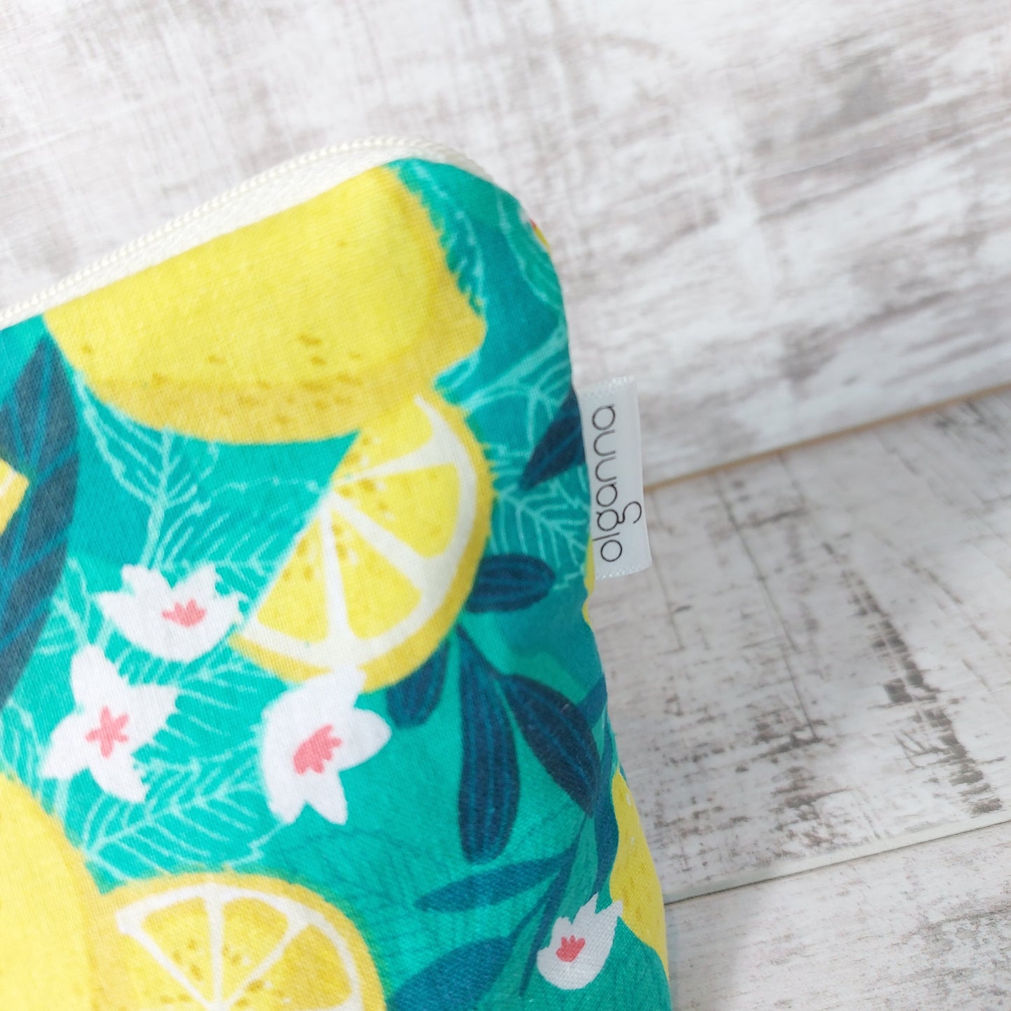 Close up view of bold green and yellow Sicilian lemon print makeup bag with side label saying 'olganna'.