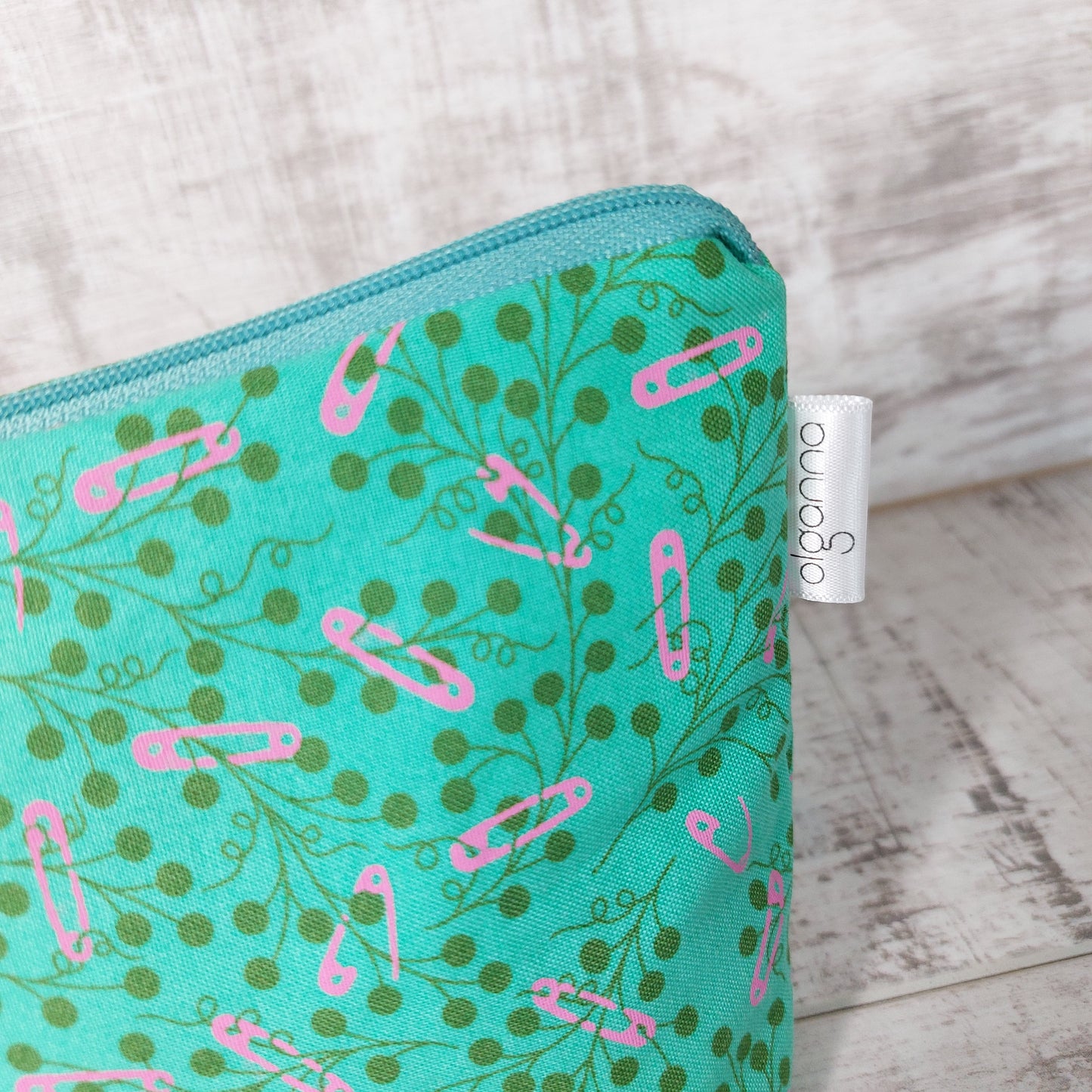 Close-up view of teal and pink floral print makeup bag with side label saying 'olganna'.