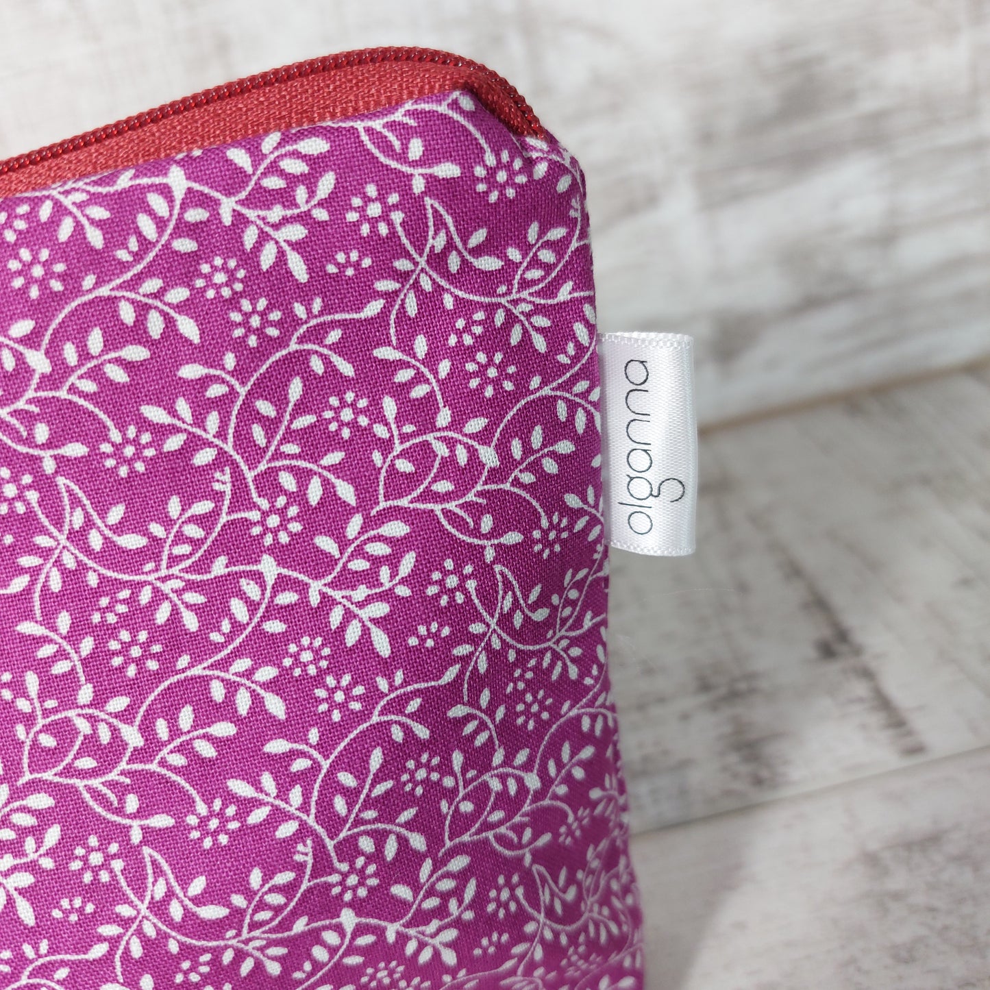 Closeup of plum ditsy floral print makeup bag with side label saying 'olganna'.