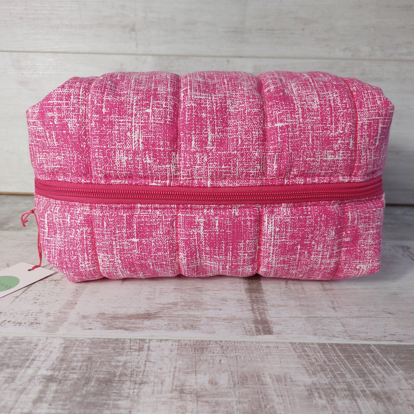 Pink quilted large toiletries bag, lying on its side to show pink zip opening.