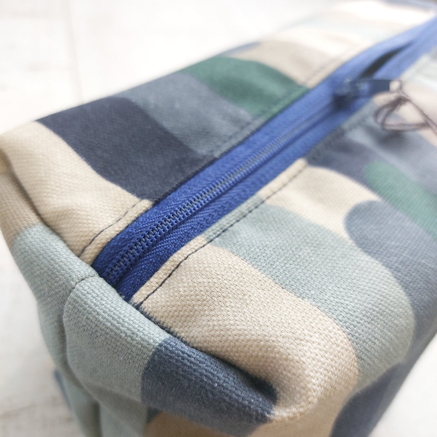 Top view of boxy zip pouch in blue and winter tones stripe pattern showing blue zip opening.