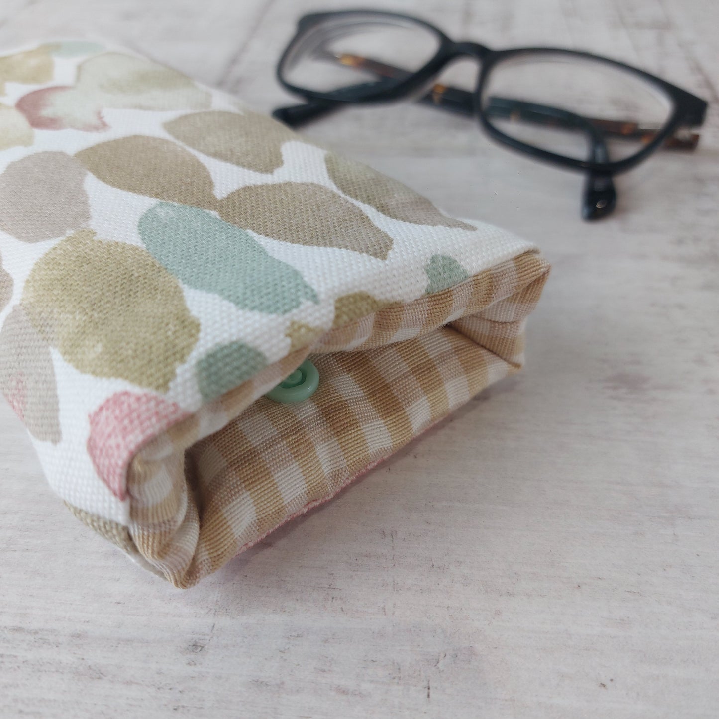 Closeup of glasses case in neutral stone pebble print with gingham lining, pictured with glasses.