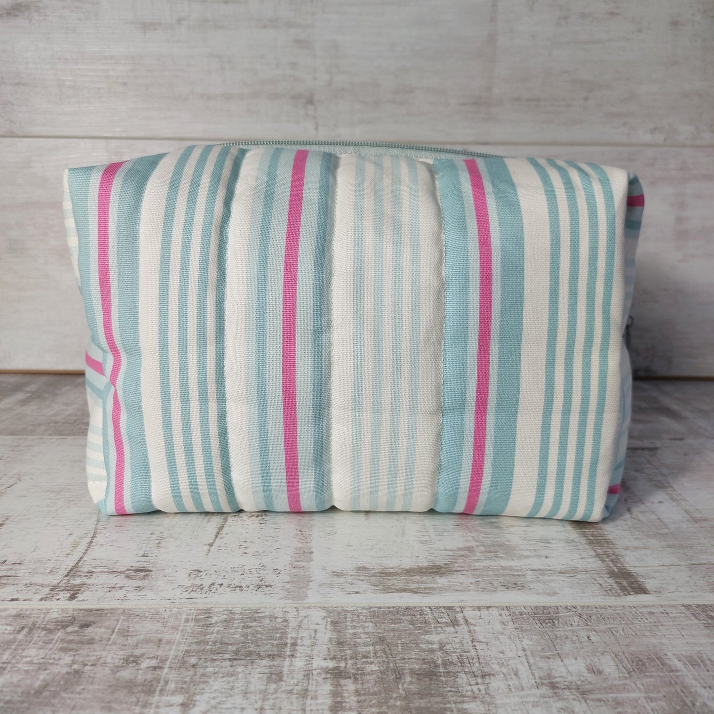 Side view of a large quilted boxy toiletries bag in pale blue, pink and white narrow stripes.