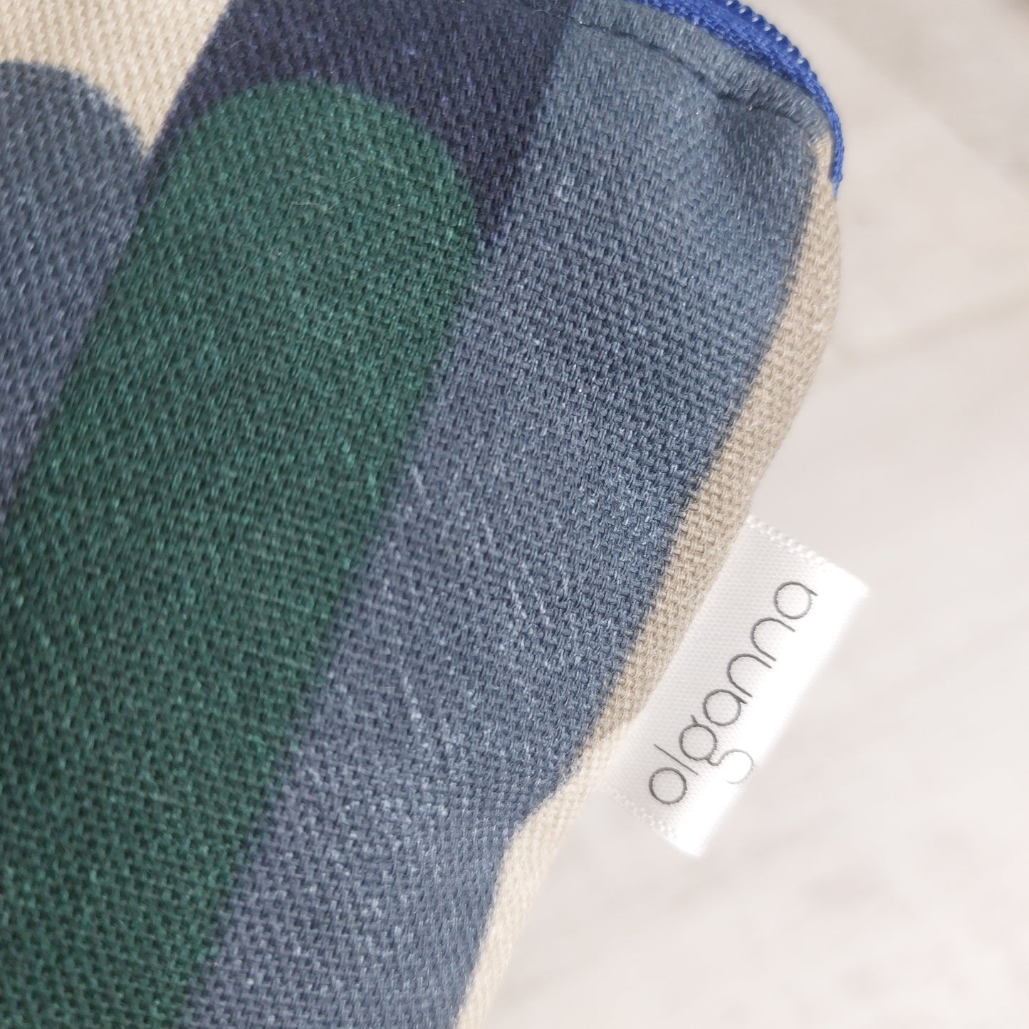 Closeup of toiletries zip bag in blue and winter tones stripe pattern with side label saying 'olganna'.