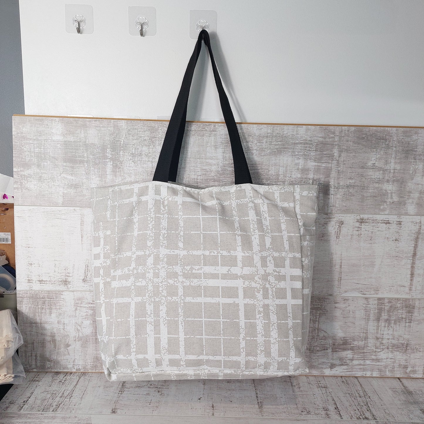 Simple modern print beach bag in neutral colours hanging from a hook.