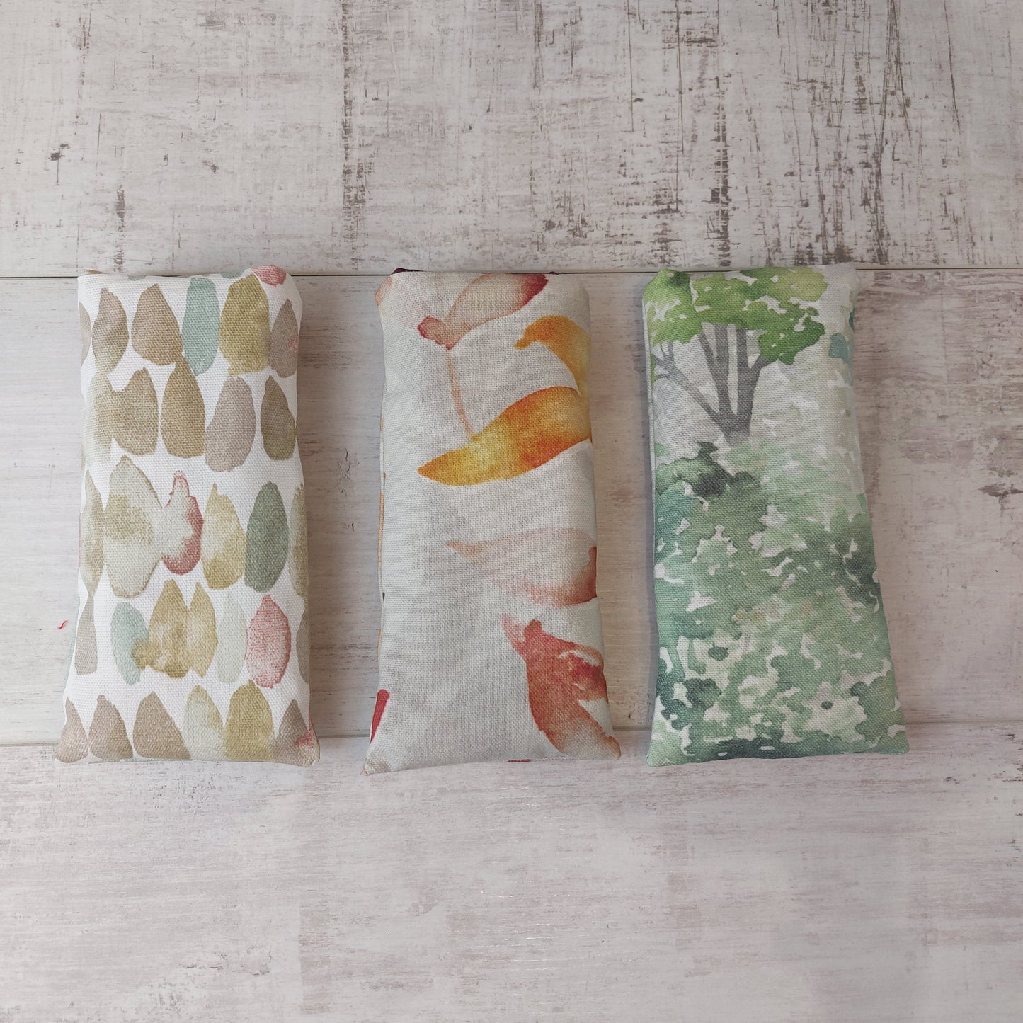 Three glasses cases in neutral stone pebble print, autumn leaves print and green watercolour tree print, pictured in a row.