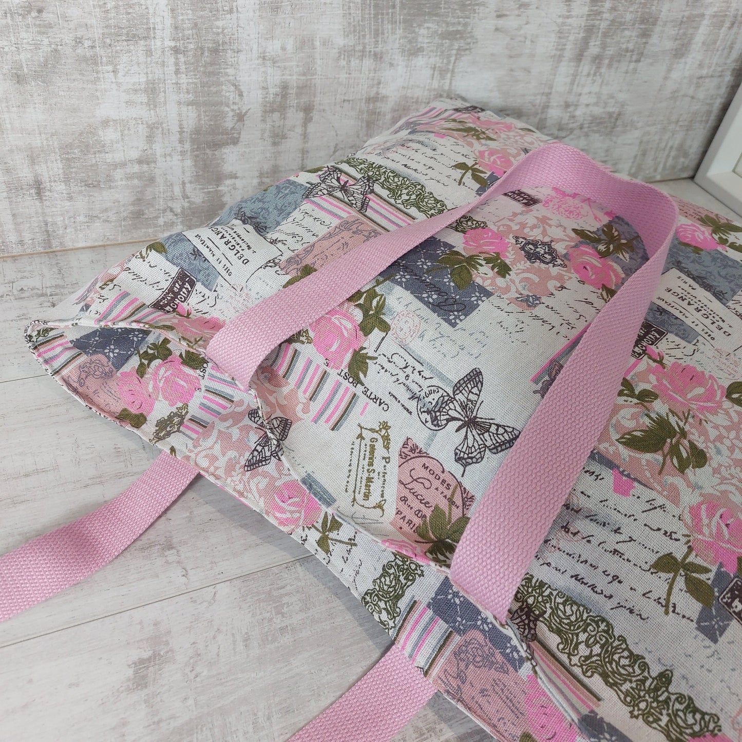 Pink and grey vintage rose and butterfly print beach bag, with deep-set zip closure, lying down.