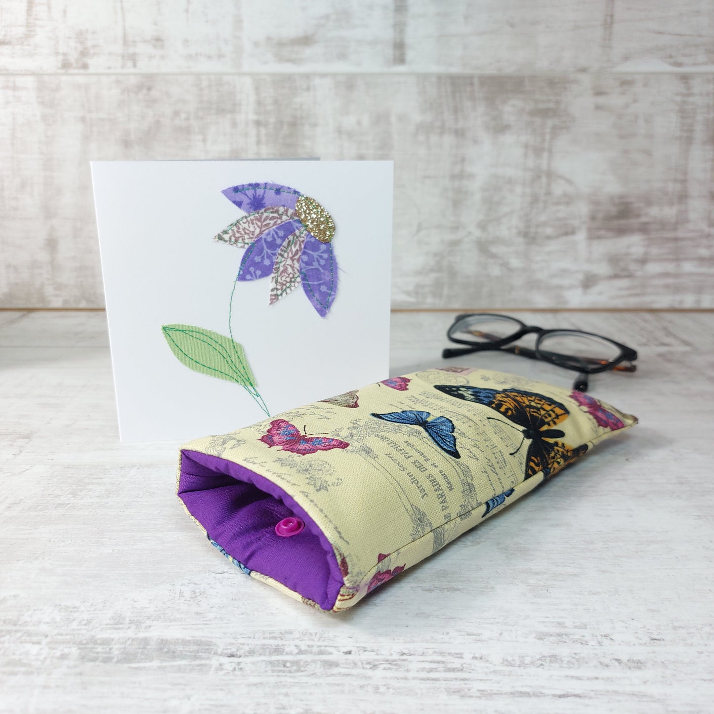 Butterfly print glasses case next to handmade greetings card featuring a flower and reading glasses.
