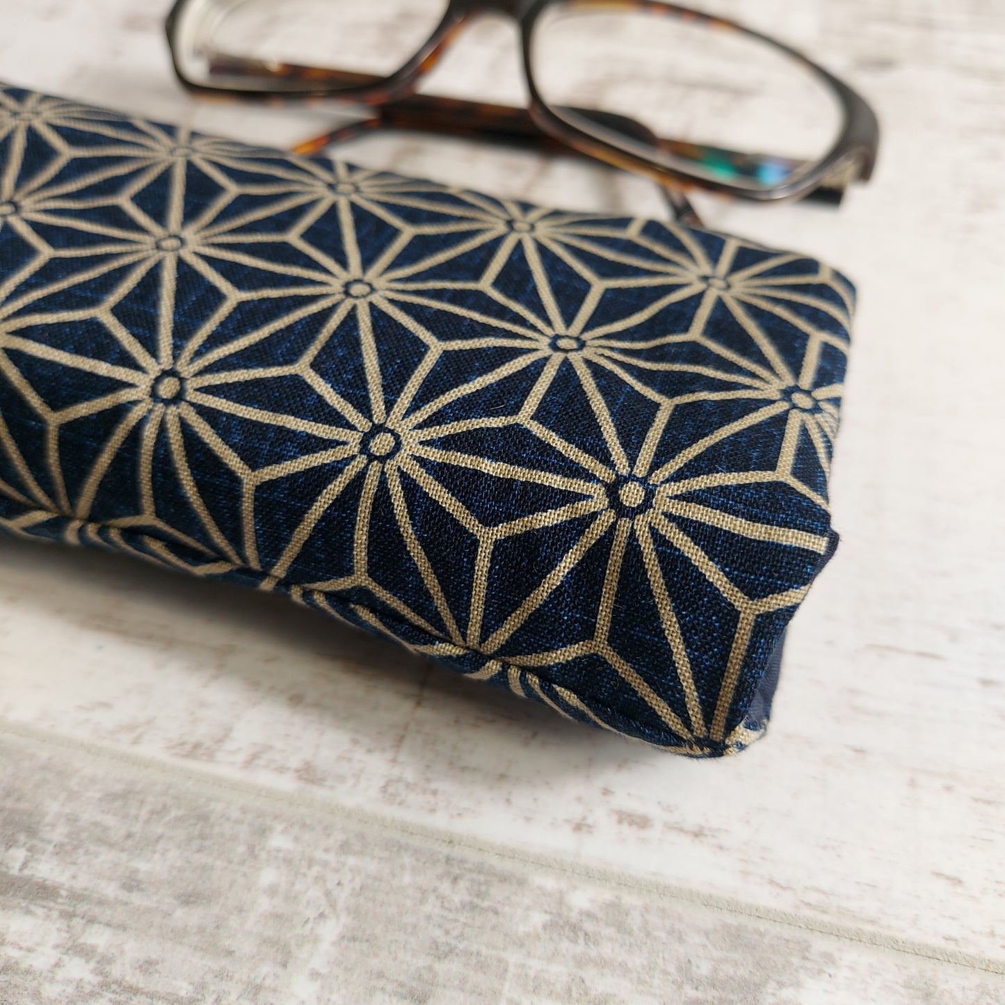 Close-up view of navy and taupe Japanese minimalist pattern glasses case with glasses in background.