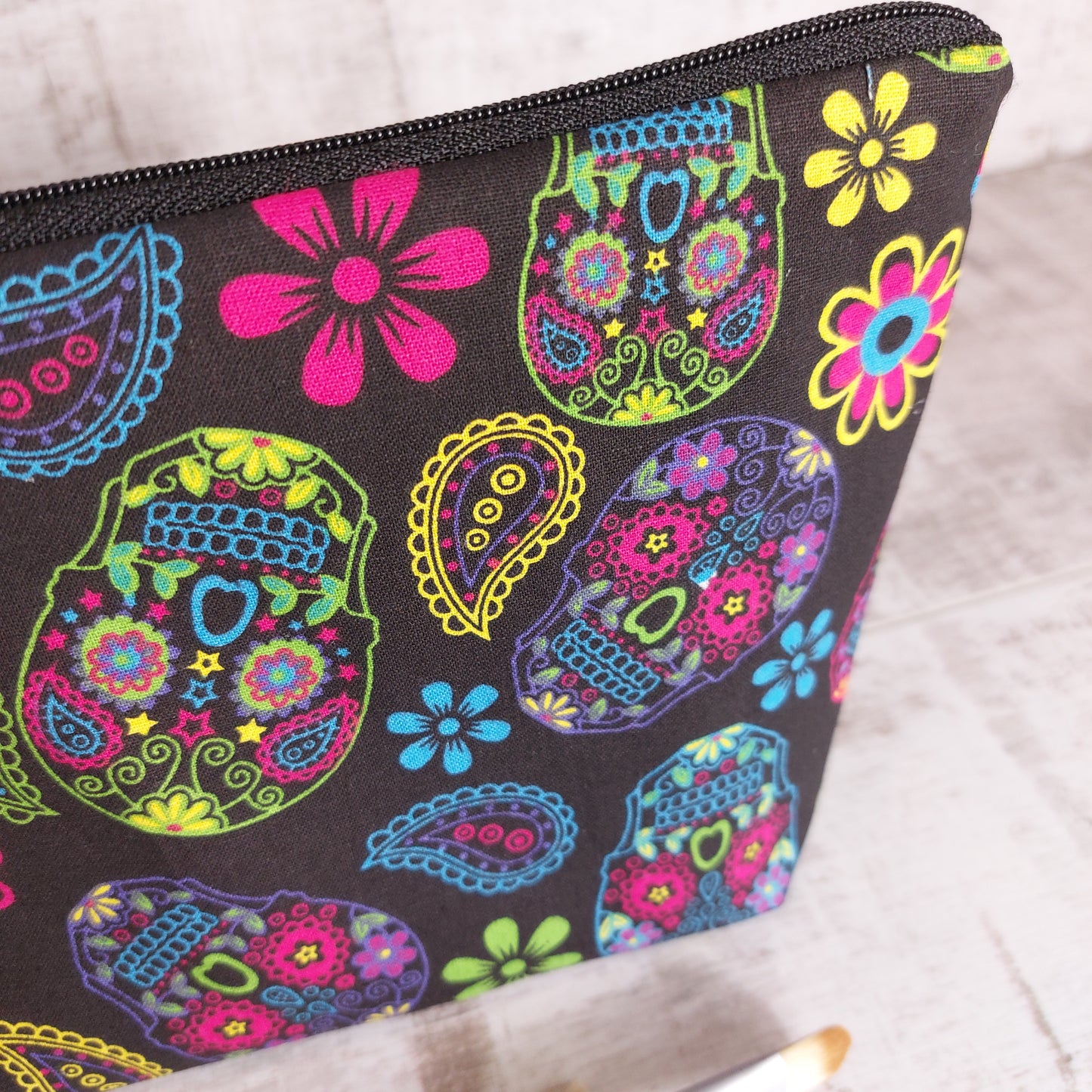 Closeup of bold and colourful sugar skulls makeup bag with black zip fastening.