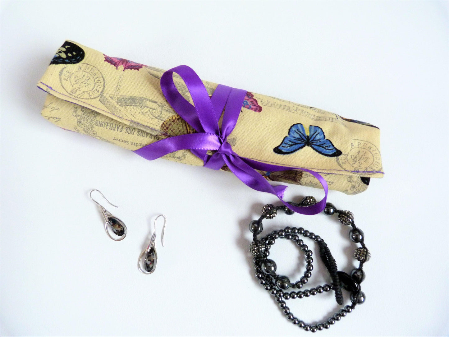 Travel jewellery organiser in vintage butterfly design, rolled with purple ribbon tie, pictured with jewellery.