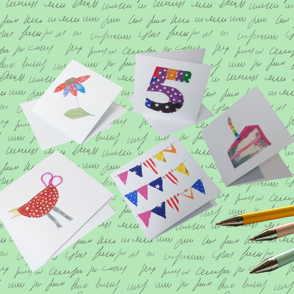 5 assorted greetings cards scattered on a mint background filled with handwriting. 3 pens also feature.