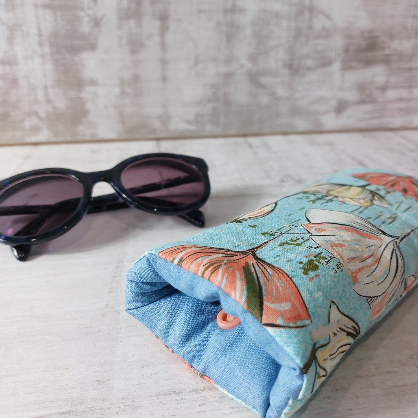 Blue stylised poppy print glasses case by Olganna, pictured with sunglasses.