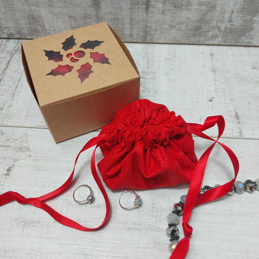 Red glitter jewellery pouch with red ribbon pull-ties, pictured with a gift box and jewellery.