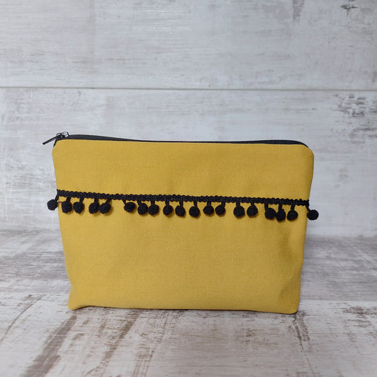 Mustard canvas makeup bag, front view, with black pom poms.