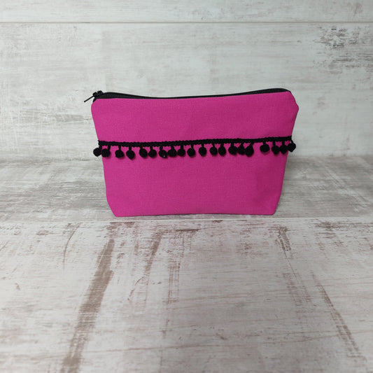 Hot pink canvas makeup bag, front view, with black pom poms.