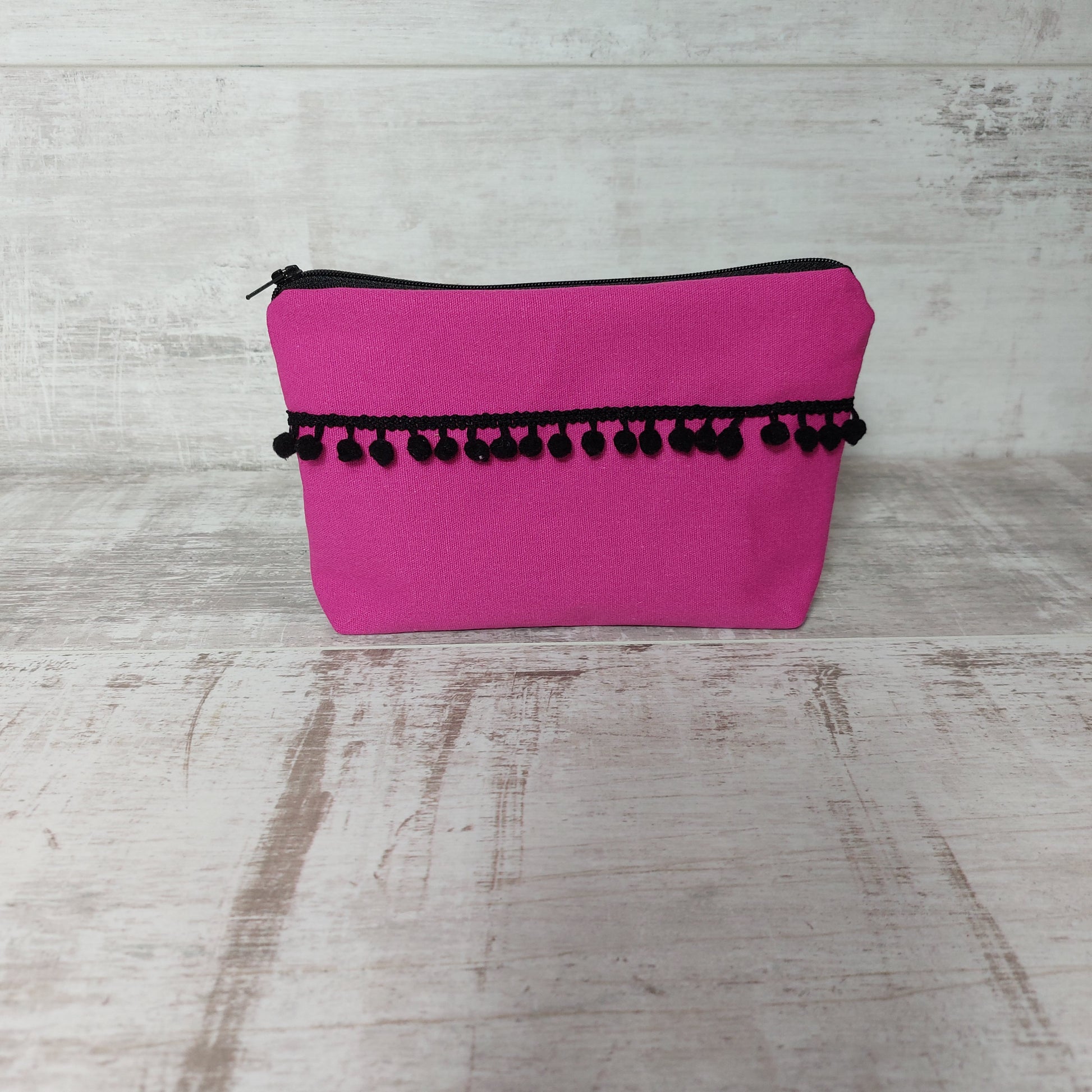 Hot pink canvas makeup bag, front view, with black pom poms.