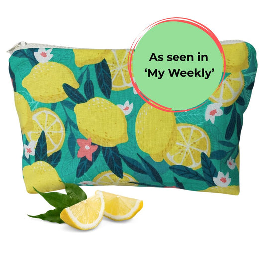 Front view of bold green and yellow Sicilian lemon print makeup bag, pictured with lemon slices and 'As seen in My Weekly' text label.