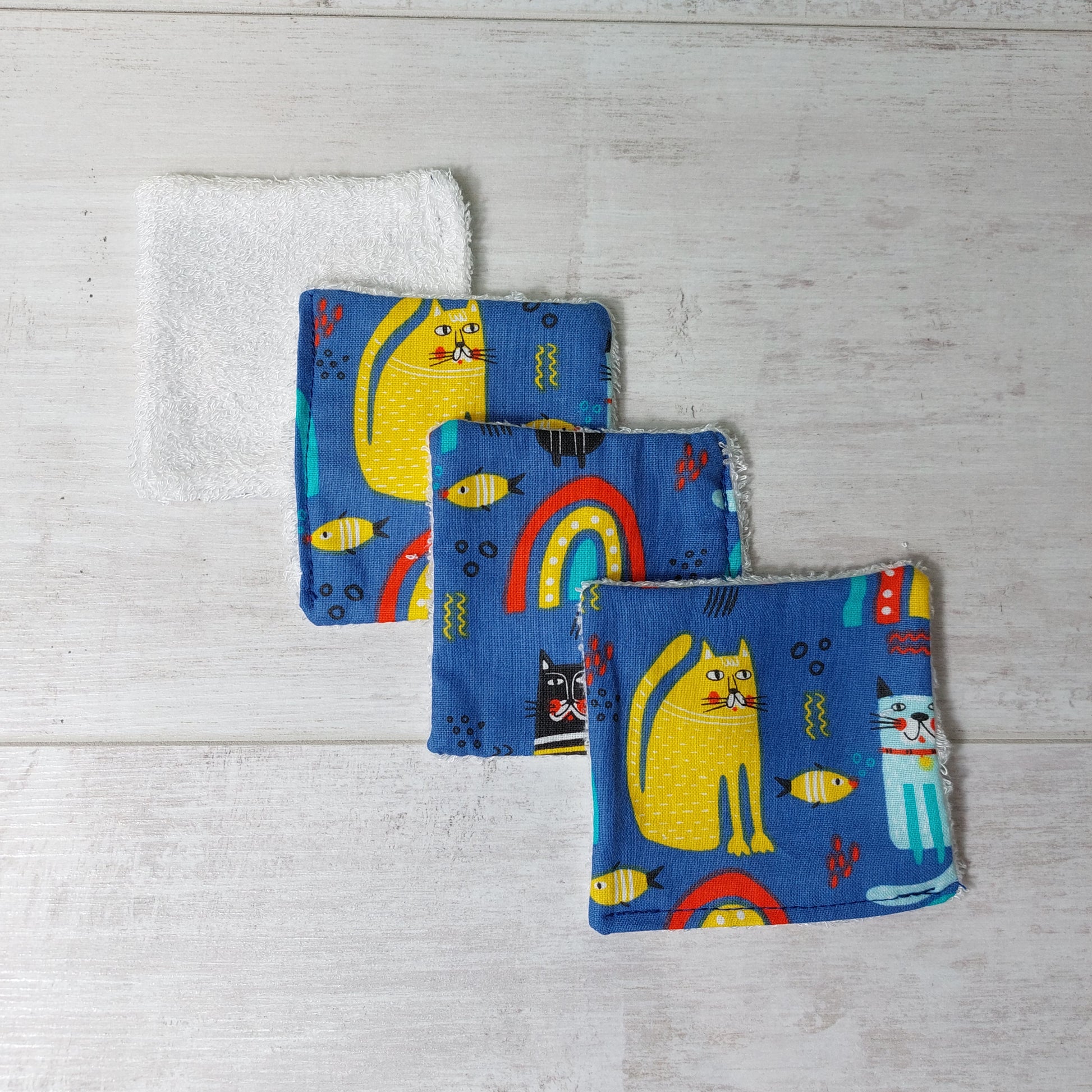 Four bamboo face wipes overlapping, in blue rainbow, cat and fish print.