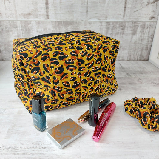 Large boxy makeup bag in leopard print pictured with leopard print scrunchie and makeup essentials.