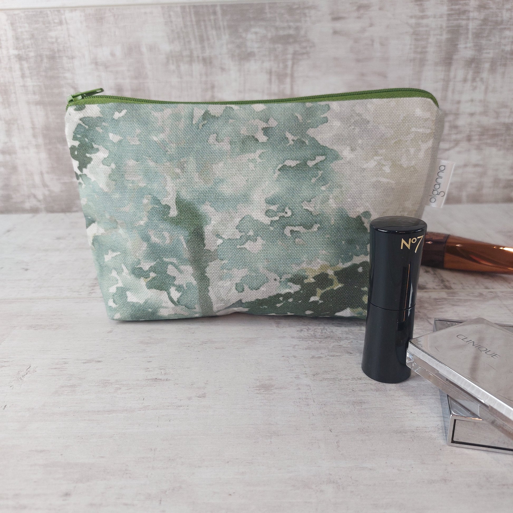 Forest green tree print makeup bag with zip, pictured with makeup and with an 'olganna' side label.