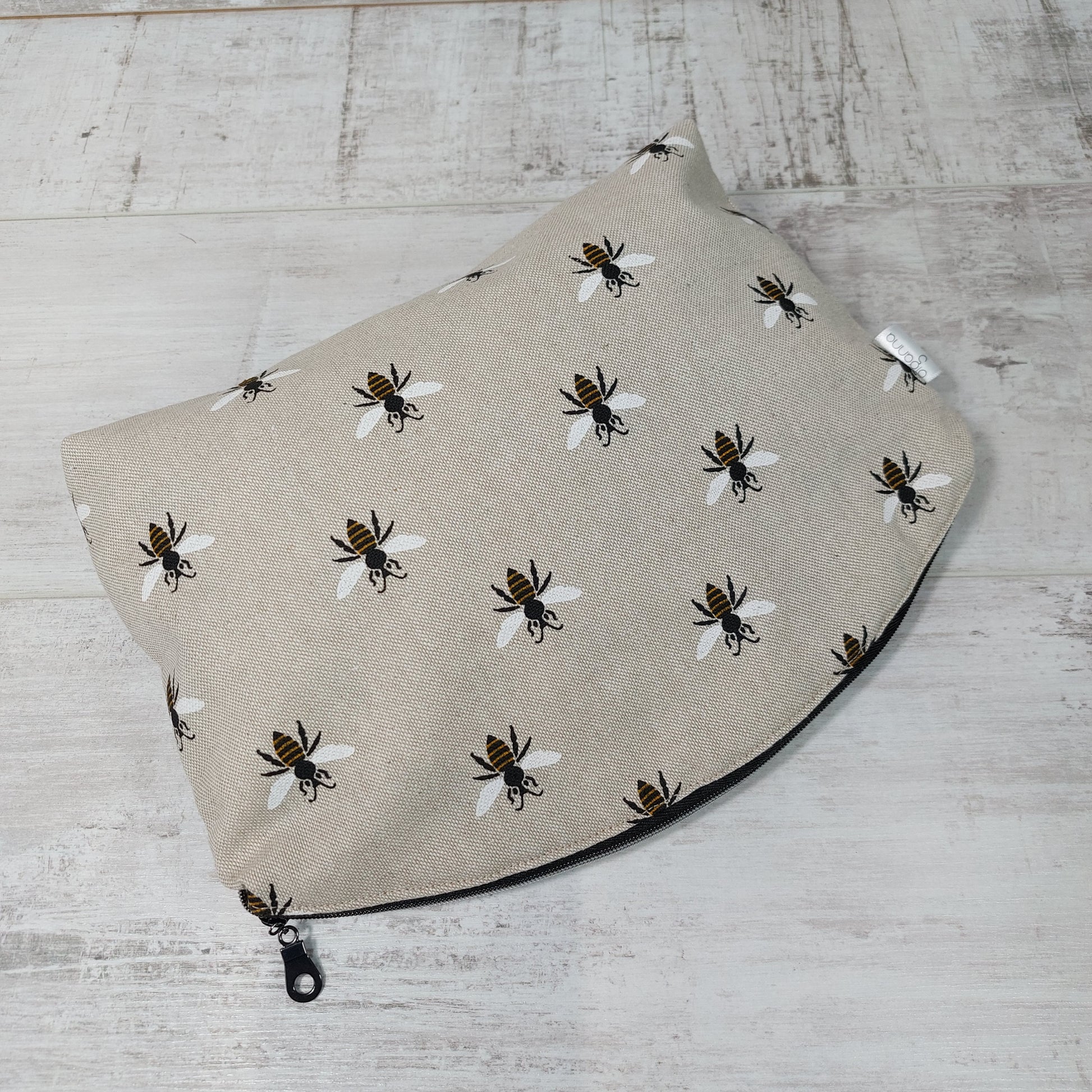 A makeup bag laid flat with a round zip fastening and repeat bee print on linen-look fabric.