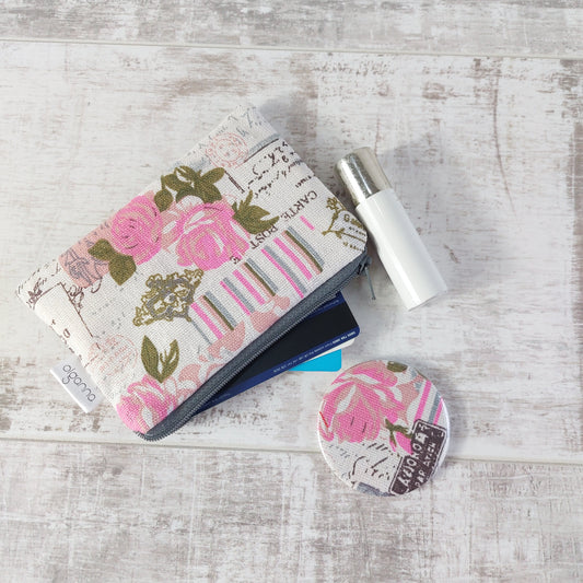 Floral vintage-style print zip purse in a soft pink Paris-inspired design open to reveal bank cards, pictured with a matching compact mirror and next to a lipstick.