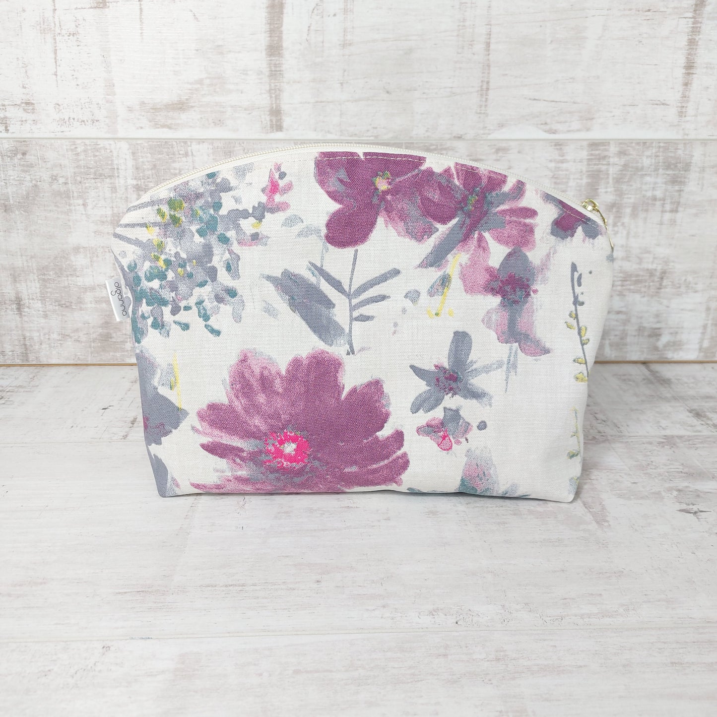 Large floral make up bag with zip fastening placed upright to display a pink and mauve floral pattern on a white background.