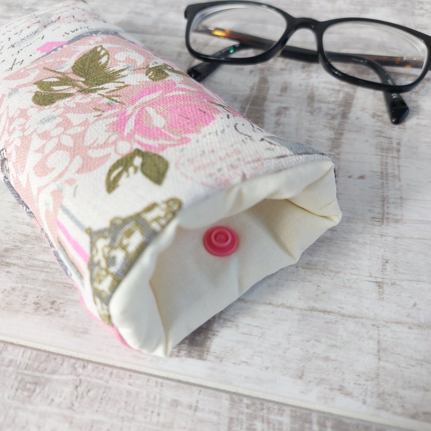Closeup of floral vintage-style print glasses case in a soft pink Paris-inspired design showing cream lining and pink snap fastening, next to a pair of glasses.