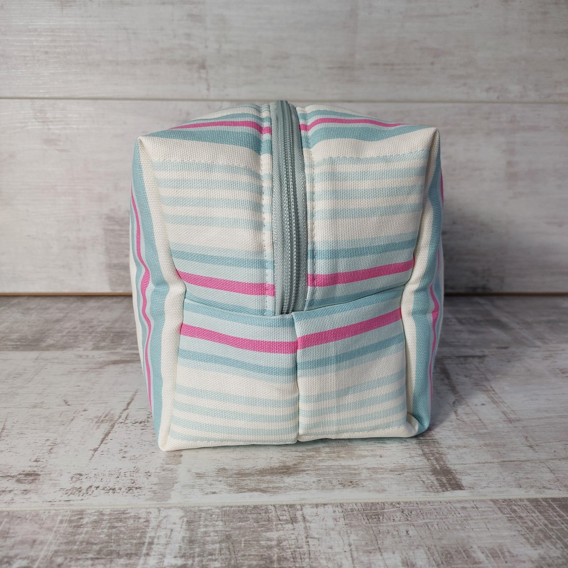End view of a large quilted boxy toiletries bag in pale blue, pink and white narrow stripes.
