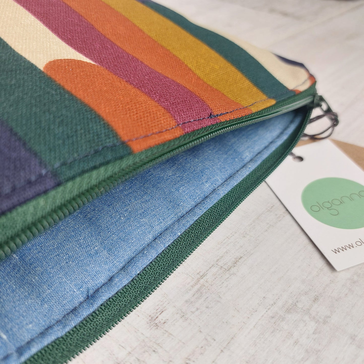 Closeup of toiletries zip bag in an autumn shades stripe pattern with green zip open to reveal blue lining.