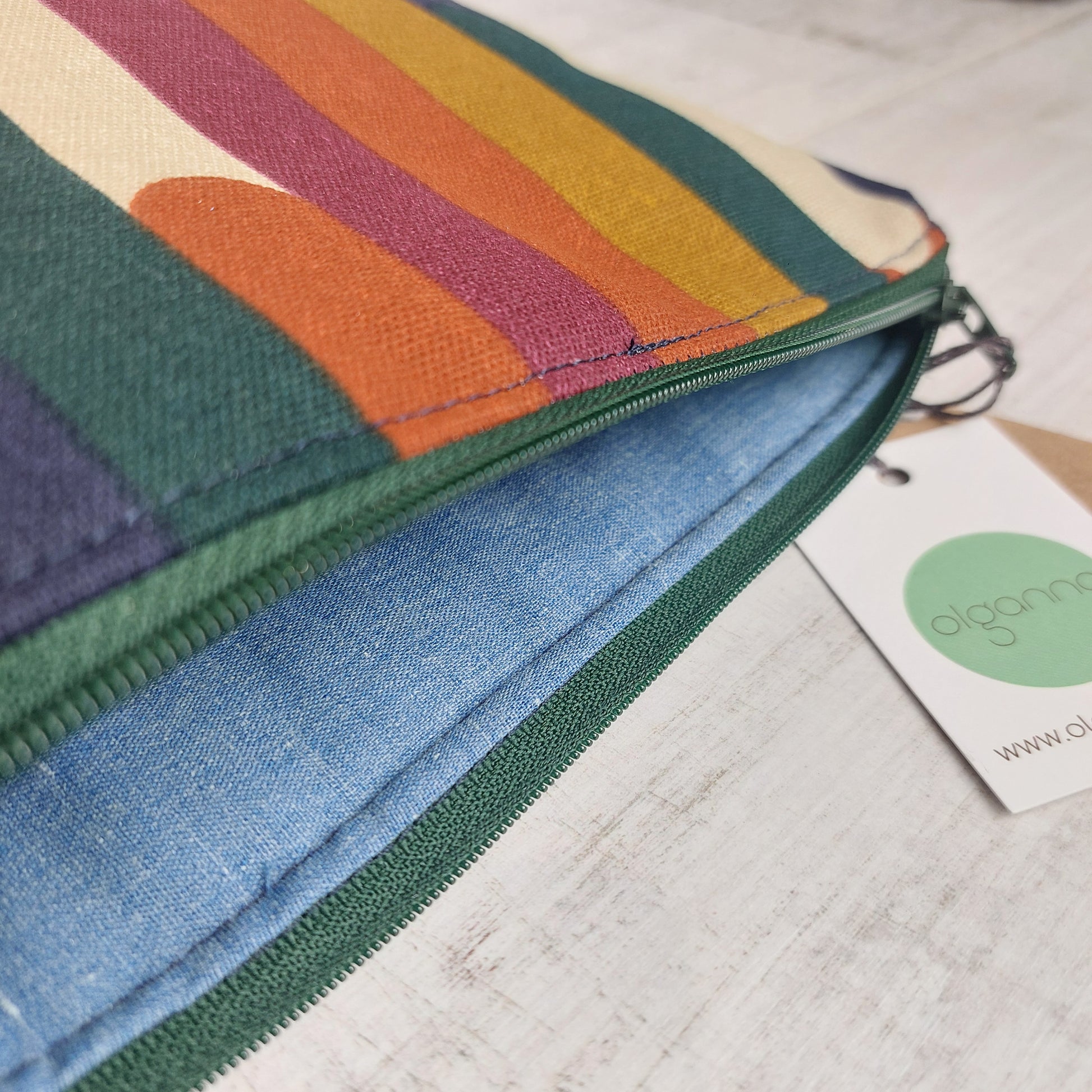 Closeup of toiletries zip bag in an autumn shades stripe pattern with green zip open to reveal blue lining.