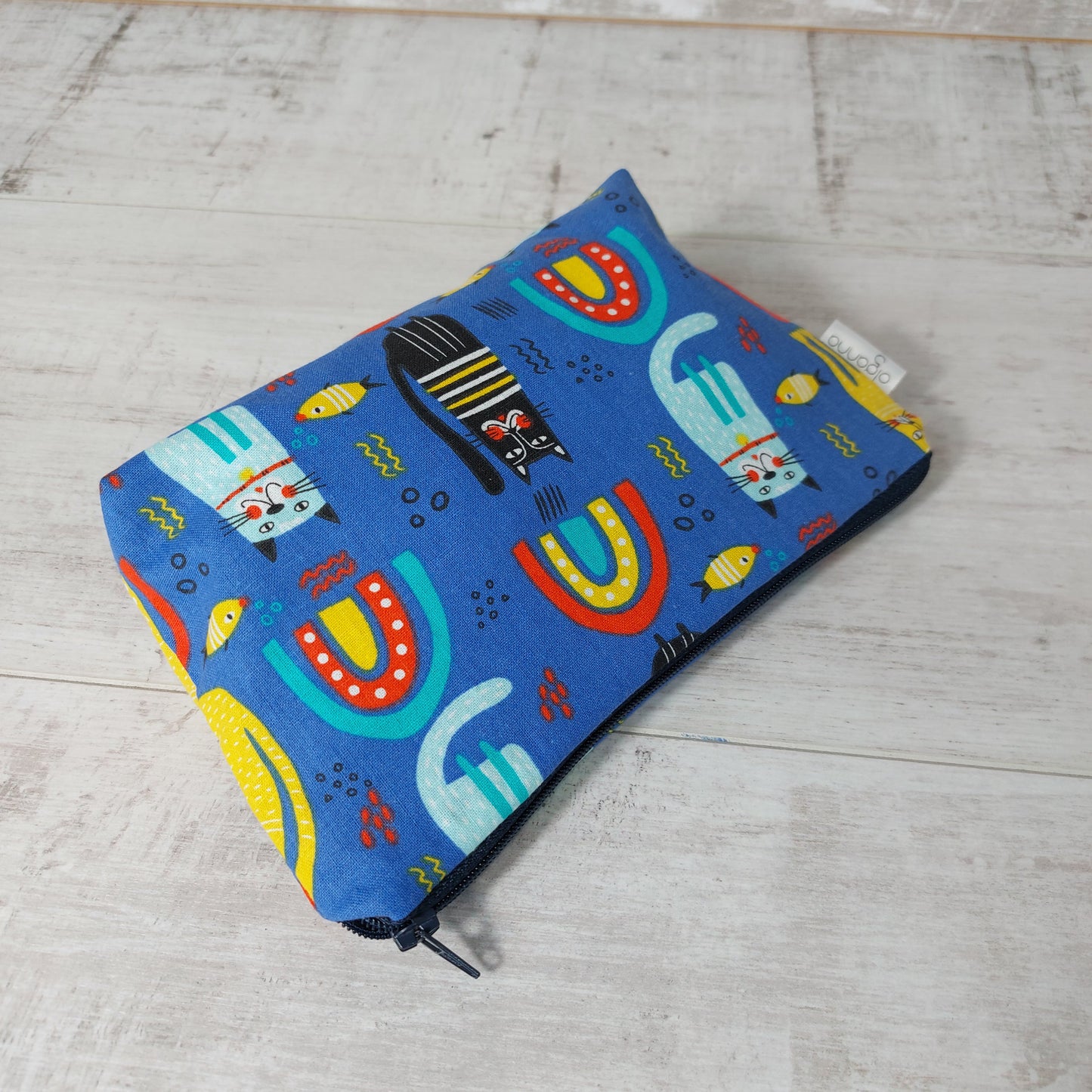 Blue rainbow, cat and fish print makeup bag, lying down. 